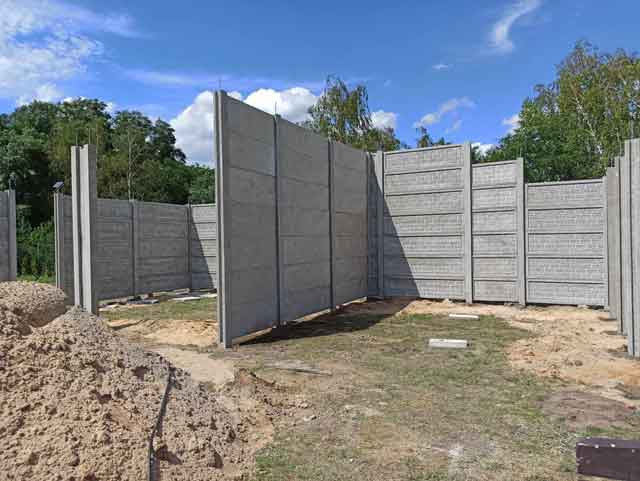 Budowa wiaty z prefabrykowanych płyt betonowych na tle zieleni i nieba.
